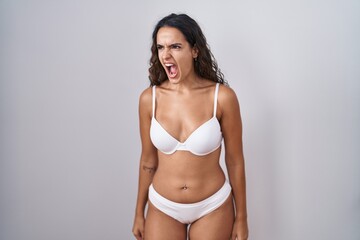 Obraz premium Young hispanic woman wearing white lingerie angry and mad screaming frustrated and furious, shouting with anger. rage and aggressive concept.