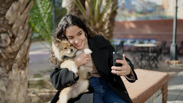 Young hispanic woman with dog smiling confident make selfie by smartphone at park