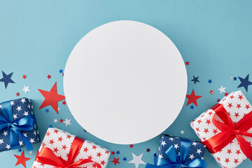 4th of July gift theme concept. Top view flat lay of gift boxes in patriotic colors, blue, red, white stars on pastel blue background with blank circle for text or advertisement