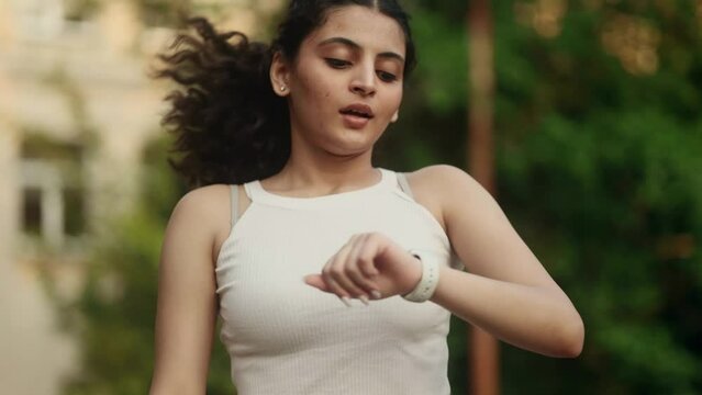 Athlete indian girl finish her running at park and happy while checking great result on smart watch tracker bracelet outdoors Smiling sporty woman jogging tracking progress in training at green city