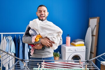 Hispanic man hanging clothes at clothesline smiling and laughing hard out loud because funny crazy...