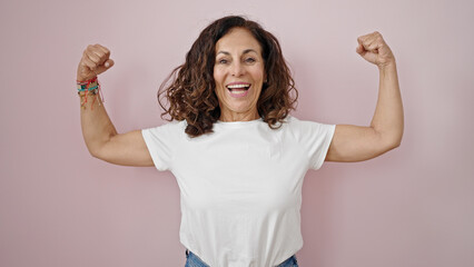 Middle age hispanic woman smiling confident doing strong gesture with arms over isolated pink...