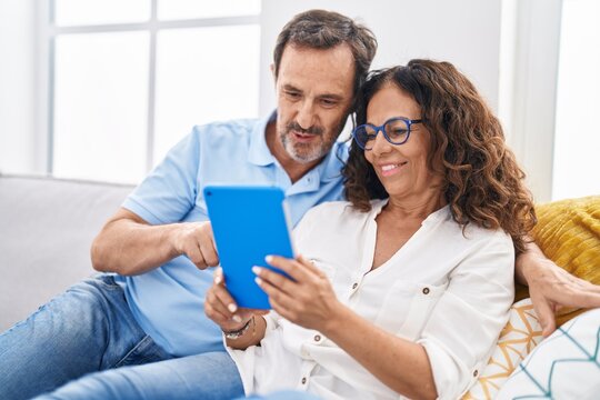Man and woman couple using touchpad sitting on sofa at home