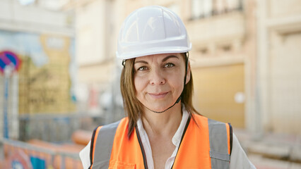 Middle age hispanic woman builder smiling confident standing at construction place