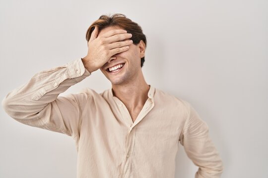 Young man standing over isolated background smiling and laughing with hand on face covering eyes for surprise. blind concept.