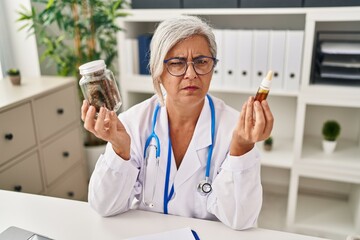 Middle age woman doctor holding cbd oil skeptic and nervous, frowning upset because of problem. negative person. - obrazy, fototapety, plakaty