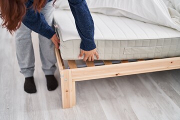 Fototapeta premium Young hispanic woman holding mattress bed at bedroom