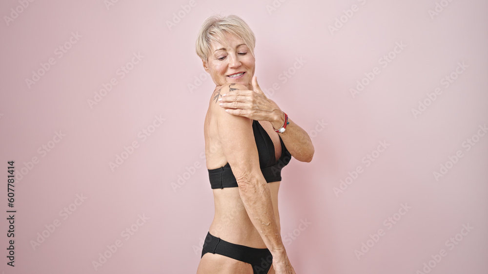 Wall mural Middle age blonde woman wearing bikini applying sunscreen over isolated pink background - Wall murals