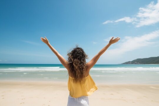 A joyful and stunning young woman raising her arms in the air at the beach, viewed from behind. AI