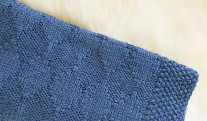 Fototapeta na wymiar Navy blue wool knitted blanket in harlequin knitting pattern on a white furry background close up