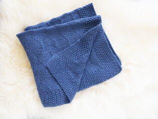 Navy blue wool knitted blanket in harlequin knitting pattern on a white furry background