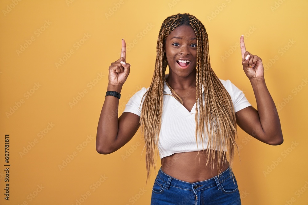 Poster african american woman with braided hair standing over yellow background smiling amazed and surprise