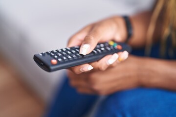 African american woman holding tv remote control sitting on sofa at home © Krakenimages.com
