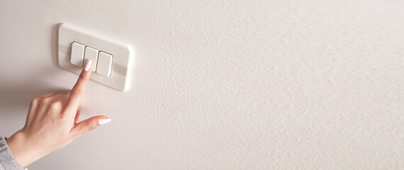 Female hand turning an electricity light switch on the wall.