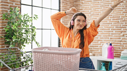 Young beautiful hispanic woman listening to music hanging clothes on clothesline dancing at laundry room
