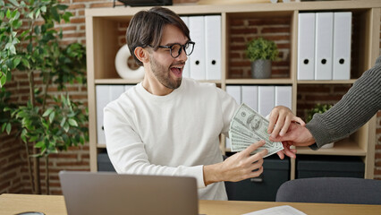 Two men business partners using laptop holding dollars at office