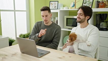 Fototapeta na wymiar Two men couple using laptop sitting on table with dog at dinning room