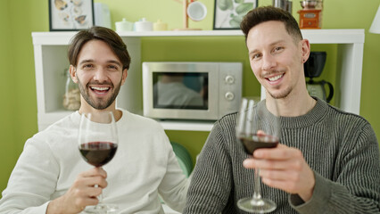 Two men couple smiling confident drinking glass of wine at dinning room