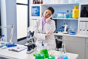 Young brunette woman working at scientist laboratory thinking looking tired and bored with depression problems with crossed arms.