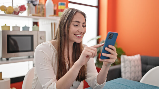 Young beautiful hispanic woman using smartphone sitting on table at dinning room