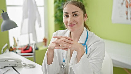 Young beautiful hispanic woman doctor smiling confident sitting on table at clinic