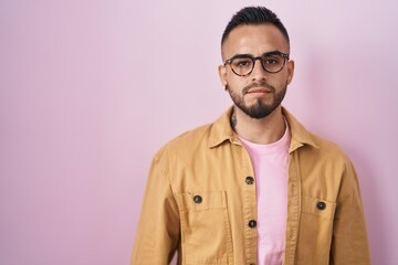 Young hispanic man standing over pink background relaxed with serious expression on face. simple and natural looking at the camera.