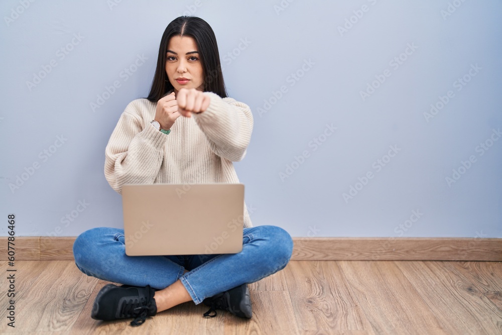 Poster Young woman using laptop sitting on the floor at home punching fist to fight, aggressive and angry attack, threat and violence