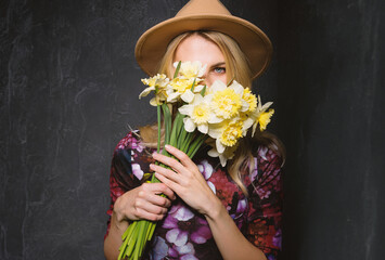 woman in dress with a bouquet of daffodils in her hands looks through a bouquet