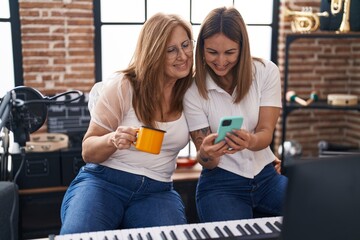 Mother and daughter musicians using smartphone drinking coffee at music studio