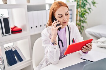 Young caucasian woman doctor using touchpad talking on smartphone at clinic