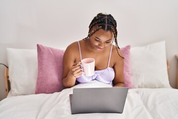 African american woman using laptop drinking coffee at bedroom