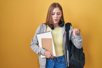 Naklejka premium Young caucasian woman wearing student backpack and holding books pointing down with fingers showing advertisement, surprised face and open mouth