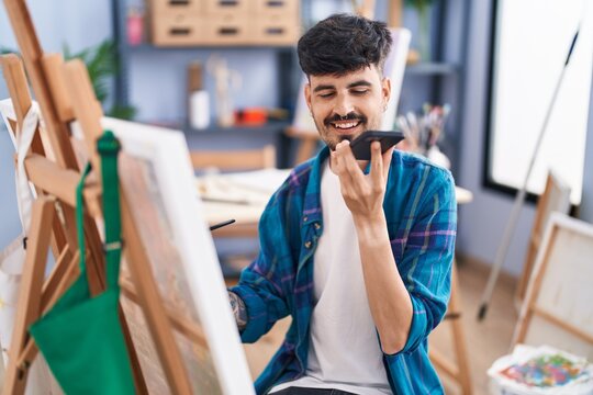 Young hispanic man artist talking on smartphone drawing at art studio