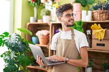 Young hispanic man florist smiling confident using laptop at flower shop