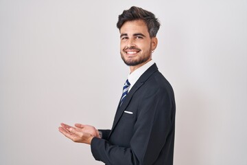 Young hispanic man with tattoos wearing business suit and tie pointing aside with hands open palms...