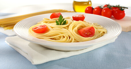 Spaghetti on a plate. yellow noodles with tomatoes and parsley leaf. cooked pasta with raw ingredients on a light background. Italian dish close up. visual recipe. mediterranean cuisine. sunny day.