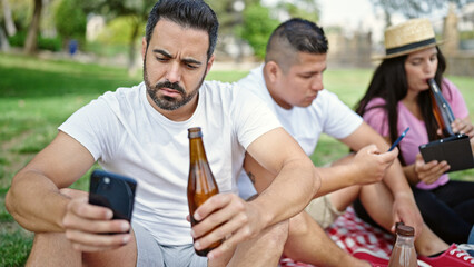 Fototapeta premium Group of people having picnic using smartphones and touchpad at park