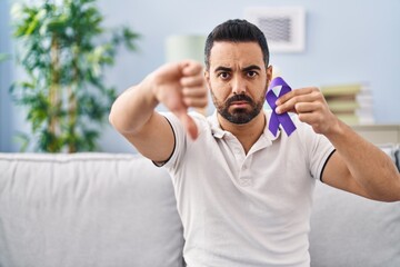 Young hispanic man with beard holding purple ribbon awareness with angry face, negative sign...