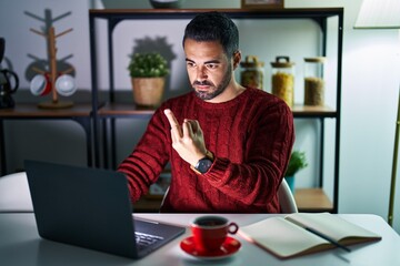 Young hispanic man with beard using computer laptop at night at home showing middle finger, impolite and rude fuck off expression