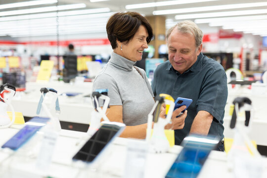 Older Couple Picking Out New Phone To Buy In Electronics Department Of Supermarket