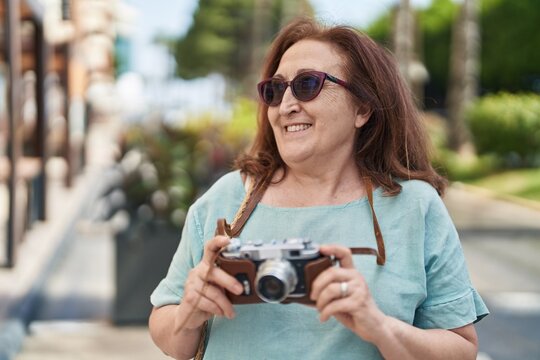 Senior woman tourist smiling confident holding camera at street