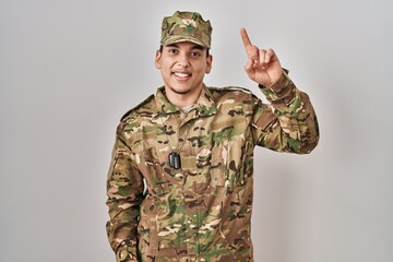 Young arab man wearing camouflage army uniform pointing finger up with successful idea. exited and...