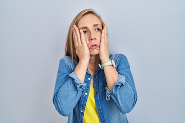 Young blonde woman standing over blue background tired hands covering face, depression and sadness, upset and irritated for problem
