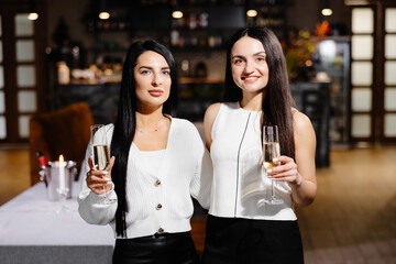 Beautiful young couple of women with glasses of champagne are celebrating in luxury restaurant