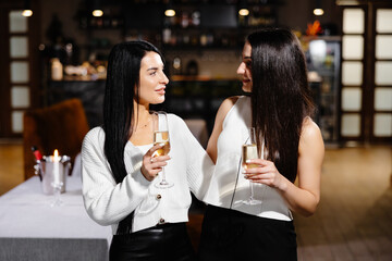 Beautiful young couple of women with glasses of champagne are celebrating in luxury restaurant