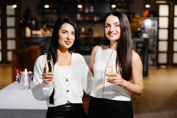 Beautiful young couple of women with glasses of champagne are celebrating in luxury restaurant