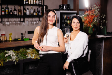 Two happy caucasian female friends drinking and talking sitting at a table in the bar of a nightclub.