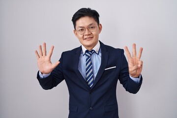 Young asian man wearing business suit and tie showing and pointing up with fingers number eight while smiling confident and happy.