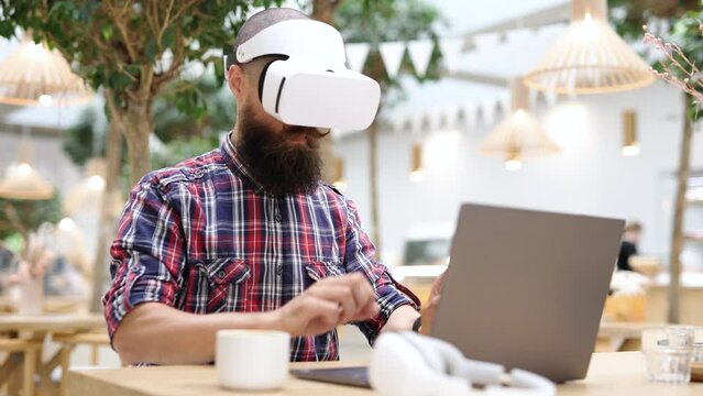 Happy man in glasses of virtual reality in cafe. Smiling male using VR helmet. Augmented reality game, future technology, 