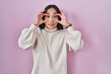 Young south asian woman standing over pink background trying to open eyes with fingers, sleepy and tired for morning fatigue